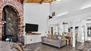Amplia sala de estar con chimenea de piedra, televisor de pantalla plana y un techo alto con ventilador.