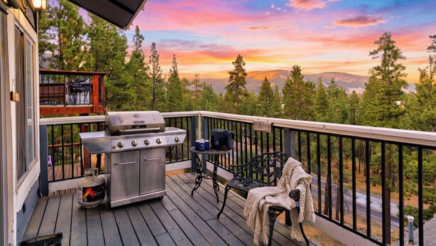 Una terraza con una parrilla, una mesa y un banco, con vistas a un área boscosa.