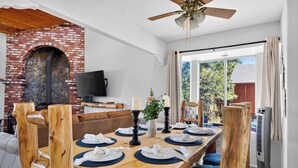 Un comedor con chimenea de ladrillo, televisor y vistas al exterior.