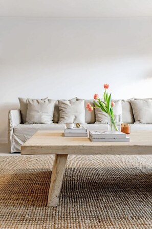 A living room with a sofa, a coffee table, books, a vase with flowers, and a candle.