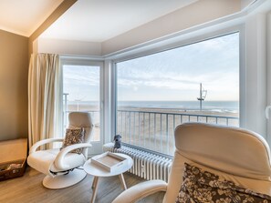 Un balcon avec vue sur la plage, deux chaises blanches, une petite table et un radiateur.