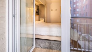 A modern bedroom with a large sliding glass door leading to a balcony, a bed with a white duvet, and a small bedside table. - Apartment in Ostend With Stunning Sea View (Koksijde)