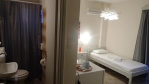 Una camera da letto piccola e luminosa con un letto singolo, un comodino e una lampada a sospensione.