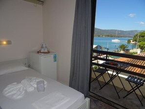 A hotel room with a bed, a small refrigerator, a table with a chair, and a balcony with a view of the sea and boats. - Villa Irene (Poros)