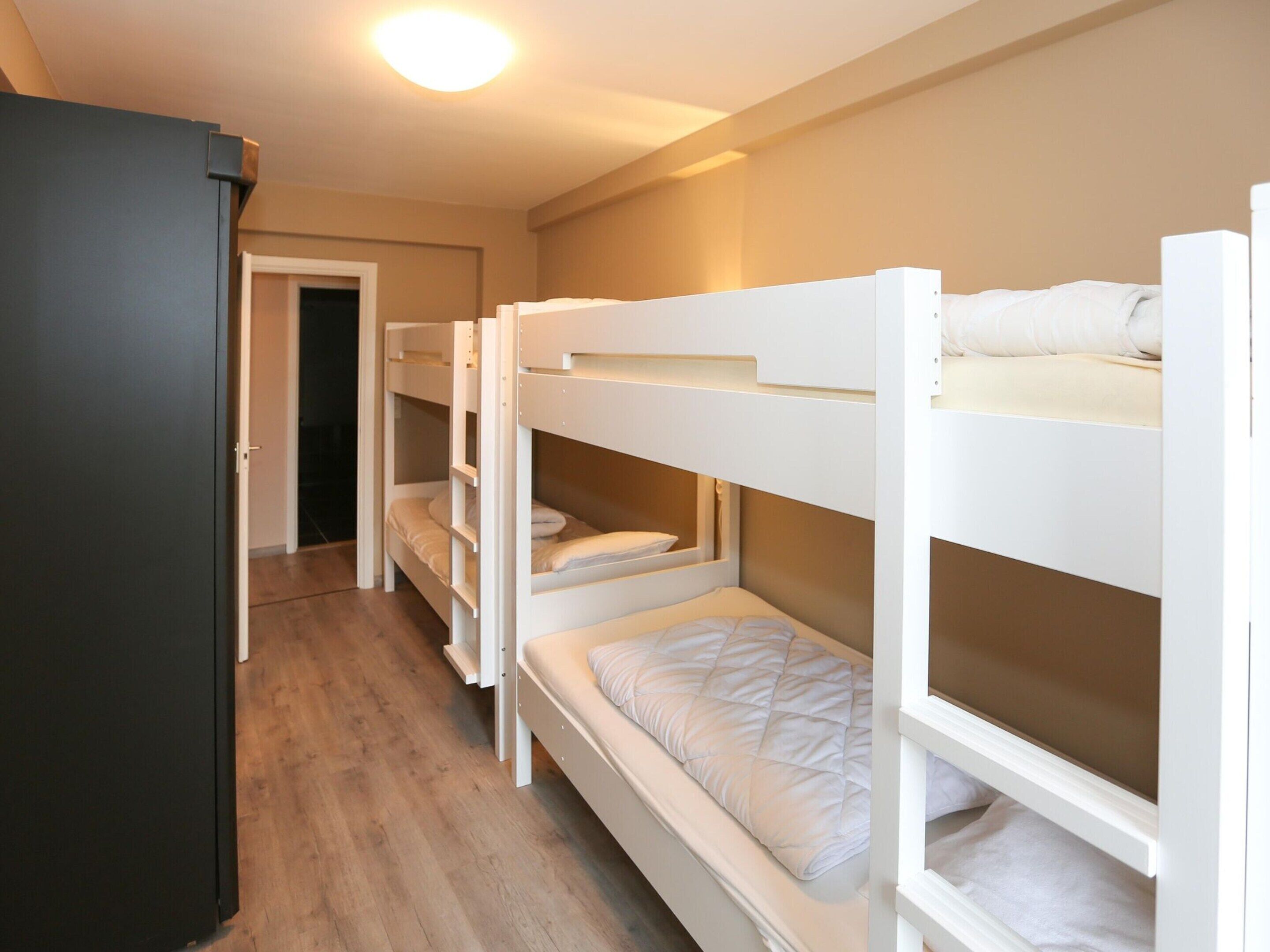 A bunk bed room with a wooden floor, a door, and a white wall.