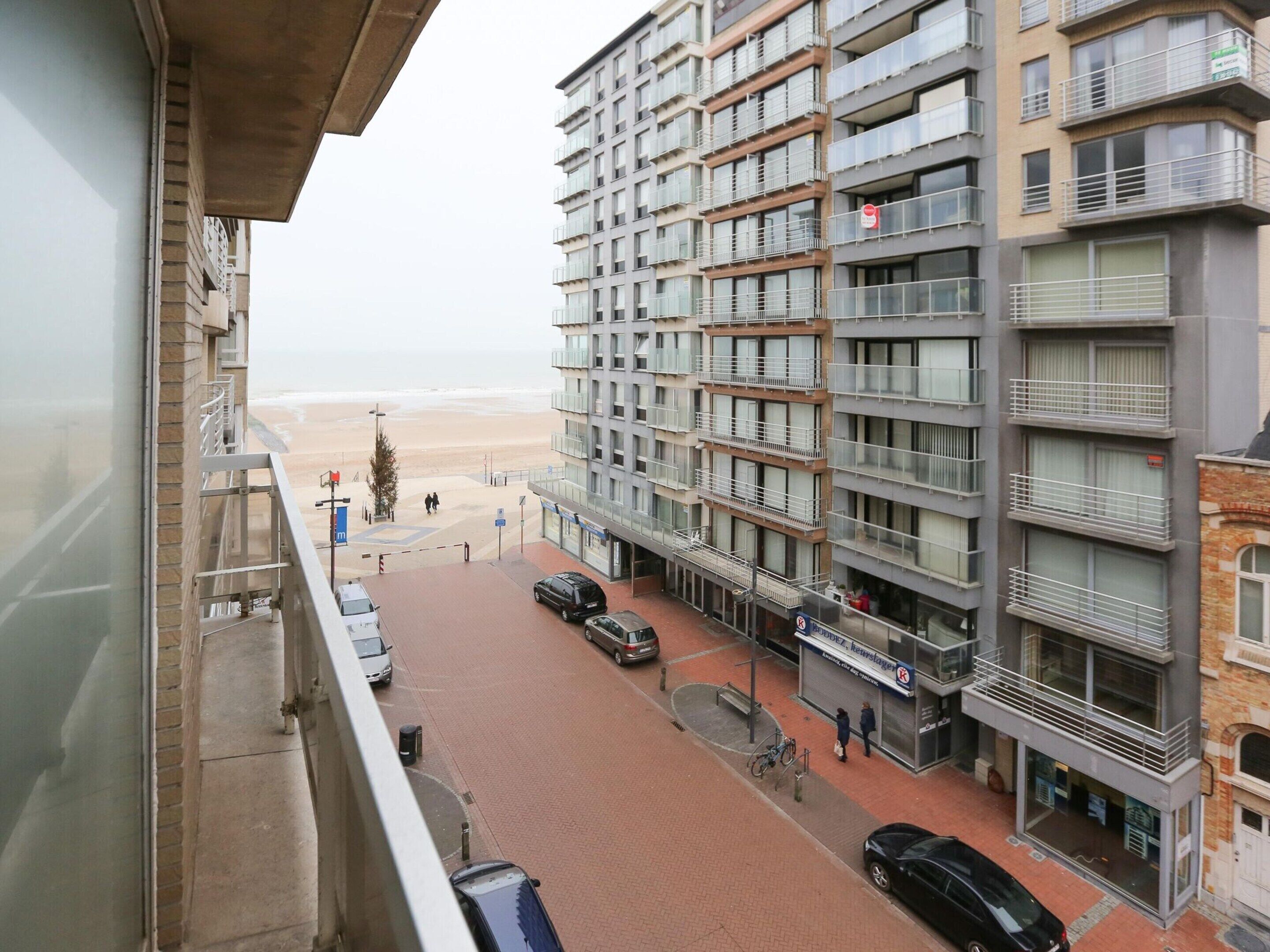 A multi-story residential building with balconies, a beach view, and a parking area with cars.