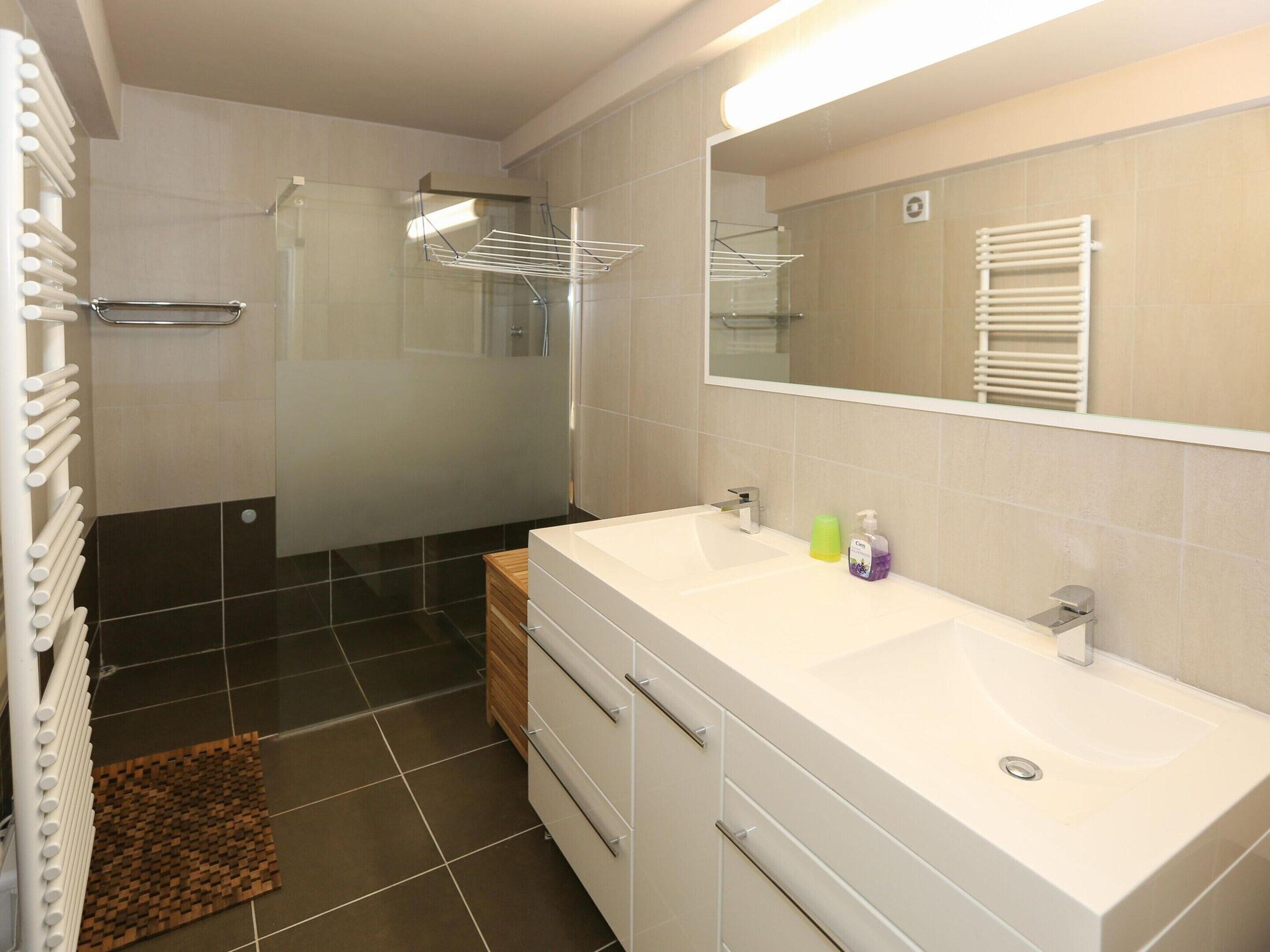 A modern bathroom with a double sink, a glass shower enclosure, and a large mirror.