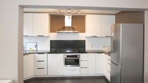 A compact kitchen with white cabinets, a stainless steel range hood, a built-in oven, and a refrigerator. - Spacious Coastal Retreat (Middelkerke)
