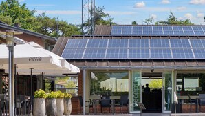 A building with a solar panel roof, outdoor seating with umbrellas, and a Coca-Cola branded sign.