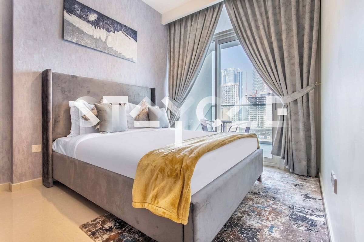 A modern hotel room with a large bed, a city view, and a grey color scheme.