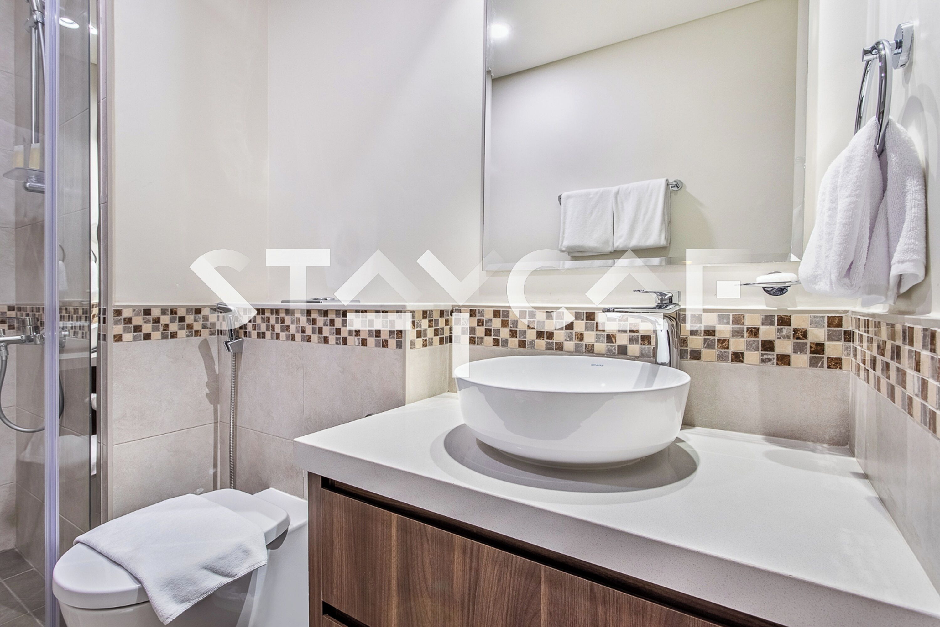 A modern bathroom with a glass shower enclosure, a white sink with a mosaic tile backsplash, and a wooden vanity.