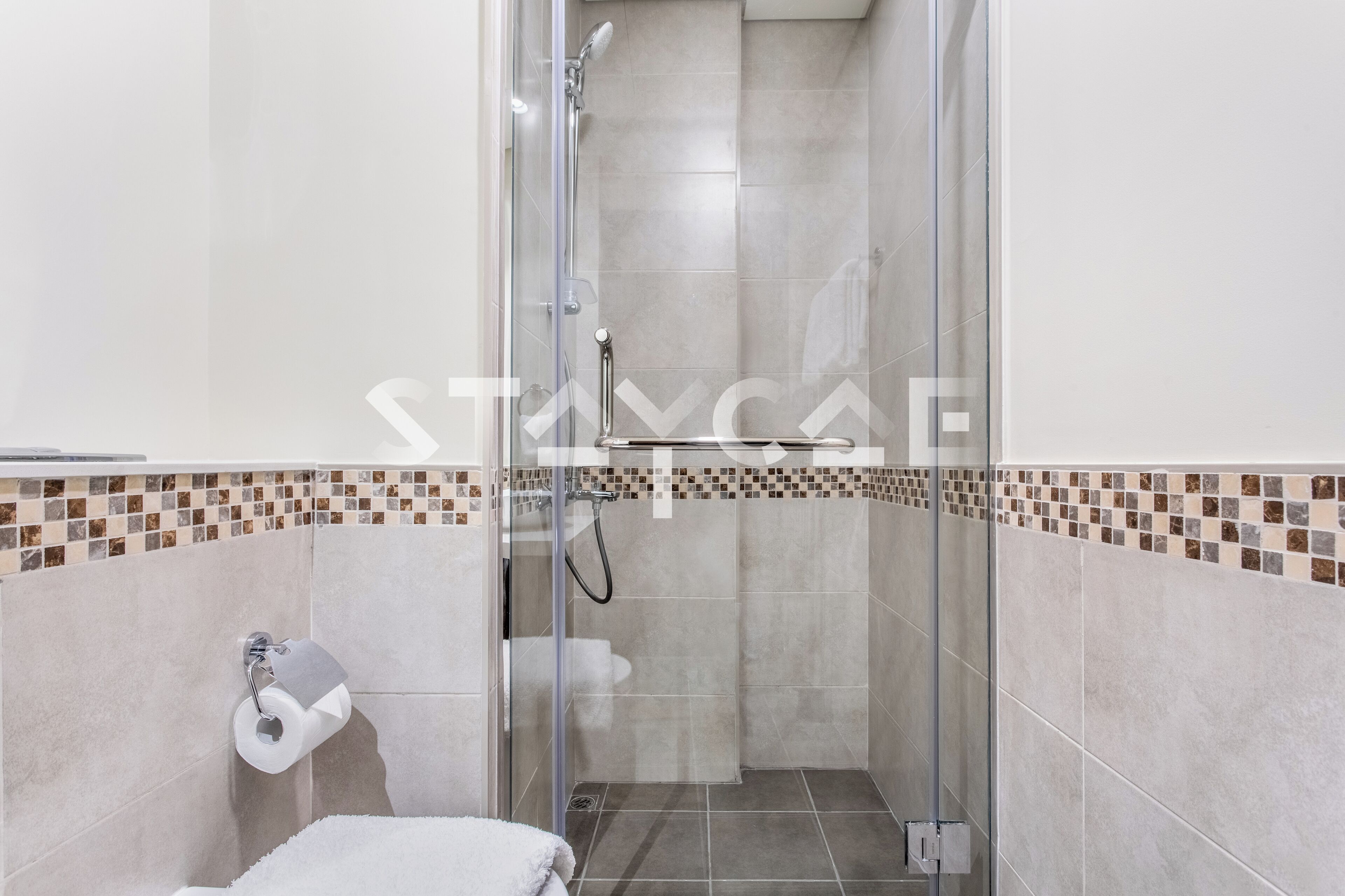 Cabina de ducha con paredes de vidrio, un cabezal de ducha, un dispensador de papel higiénico y piso de baldosas.