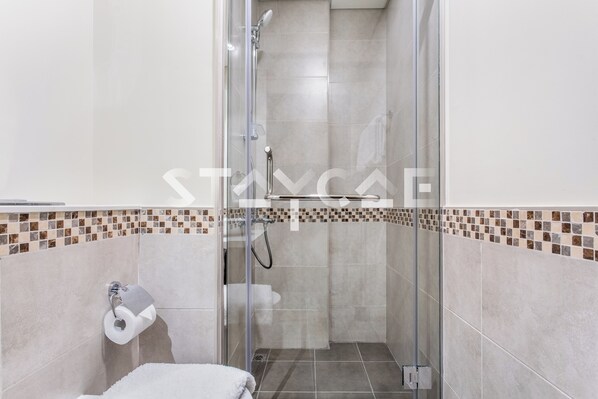 A glass-enclosed shower stall with a showerhead, a toilet paper holder, and a tiled floor.