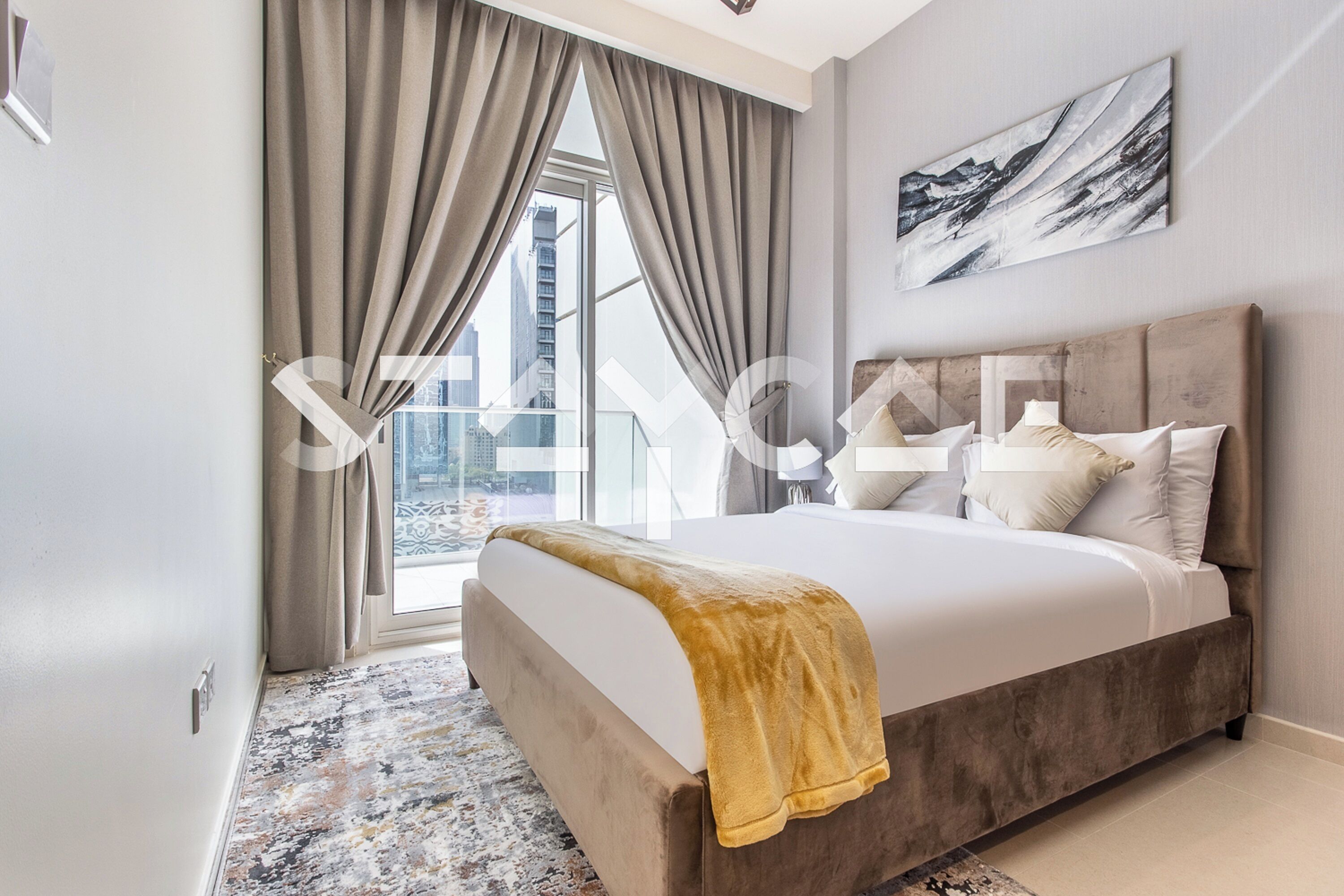 A modern bedroom with a large bed, a view of the city, and a painting on the wall.