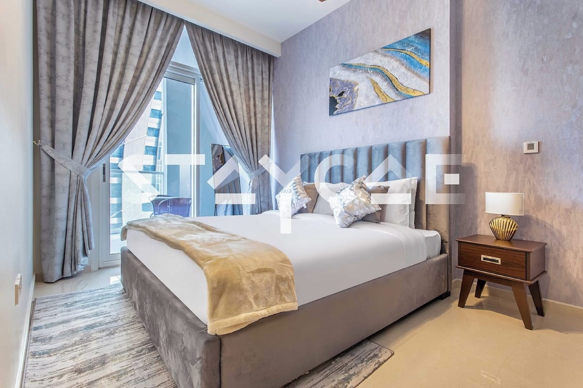 A modern bedroom with a large bed, a nightstand, a painting, and a view of the city.