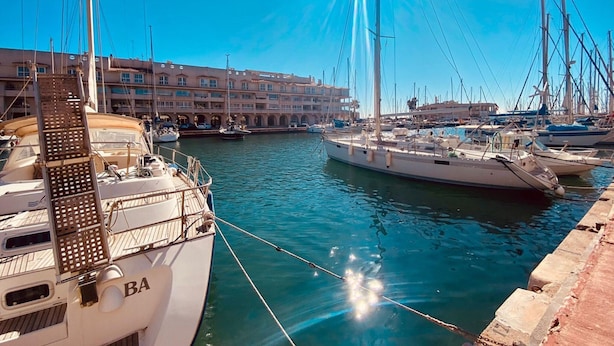 A marina with multiple boats docked, a clear blue sky, and a building with balconies in the background. - Nice Apartment in the Marina of Almerimar (El Ejido)