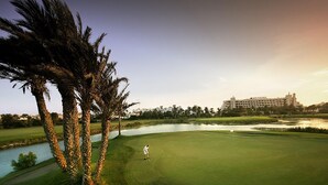 A golf course with a water hazard, palm trees, and a building in the background. - Nice Apartment in the Marina of Almerimar (El Ejido)