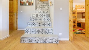 Un escalier orné de carreaux décoratifs, une porte en bois et, au fond, un lit superposé.