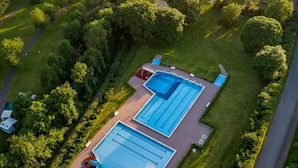 Vue aérienne d’une propriété dotée de deux piscines, entourée d’une végétation luxuriante et bordée d’une route.