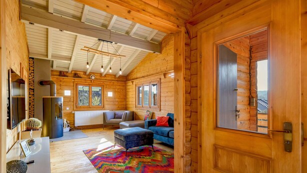 L’intérieur d’une cabane en rondins, avec un salon accueillant, une cheminée et une grande fenêtre.