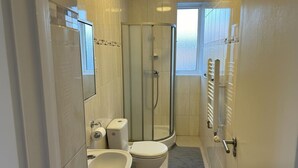 Casa de banho compacta com sanita, bidé e cabine de duche em vidro.