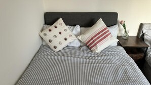 Cama bem arrumada com roupa de cama listrada e dois travesseiros, um com padrão de bolinhas e outro listrado.