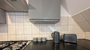 A kitchen with a gas stove, a kettle, and three containers labeled tea, sugar, and coffee. - Oak Wembley Stadium Serviced Apartment by Edens (Wembley)