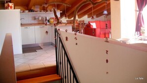 Una cocina con vigas de madera, un comedor con sofá rojo y una escalera con barandilla.