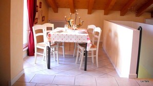 Un comedor con techo de madera, sillas blancas, una mesa con mantel floral y una cortina roja.