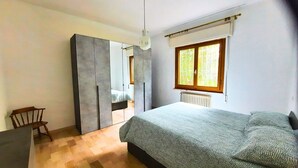 A bedroom with a bed, a wooden chair, a wardrobe, a radiator, and a window with blinds. - Olive Grove Garden House With Mountain View Close to Forte dei Marmi (Ripa- Pozzi-Ponterosso)