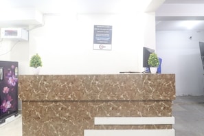 Un comptoir d’accueil avec un plateau en marbre, une petite plante en pot et un panneau indiquant un numéro de téléphone.