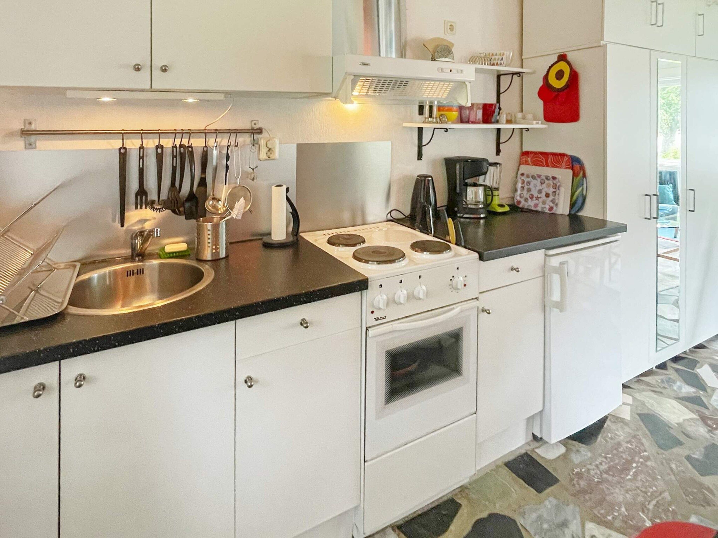 Una cocina con armarios blancos, un lavaplatos de acero inoxidable, una estufa y diversos utensilios de cocina.