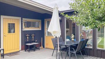 Una terraza con mesa y sillas, una sombrilla blanca y una puerta con ventanal.