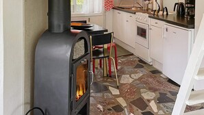 Une cuisine avec un poêle à bois, un sol carrelé et un réfrigérateur blanc.