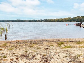 Un lago tranquilo con orilla arenosa, un bote y una colina boscosa al fondo.