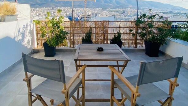Een terras buiten met een tafel en stoelen, omringd door plantenbakken en een uitzicht op een stadsbeeld.