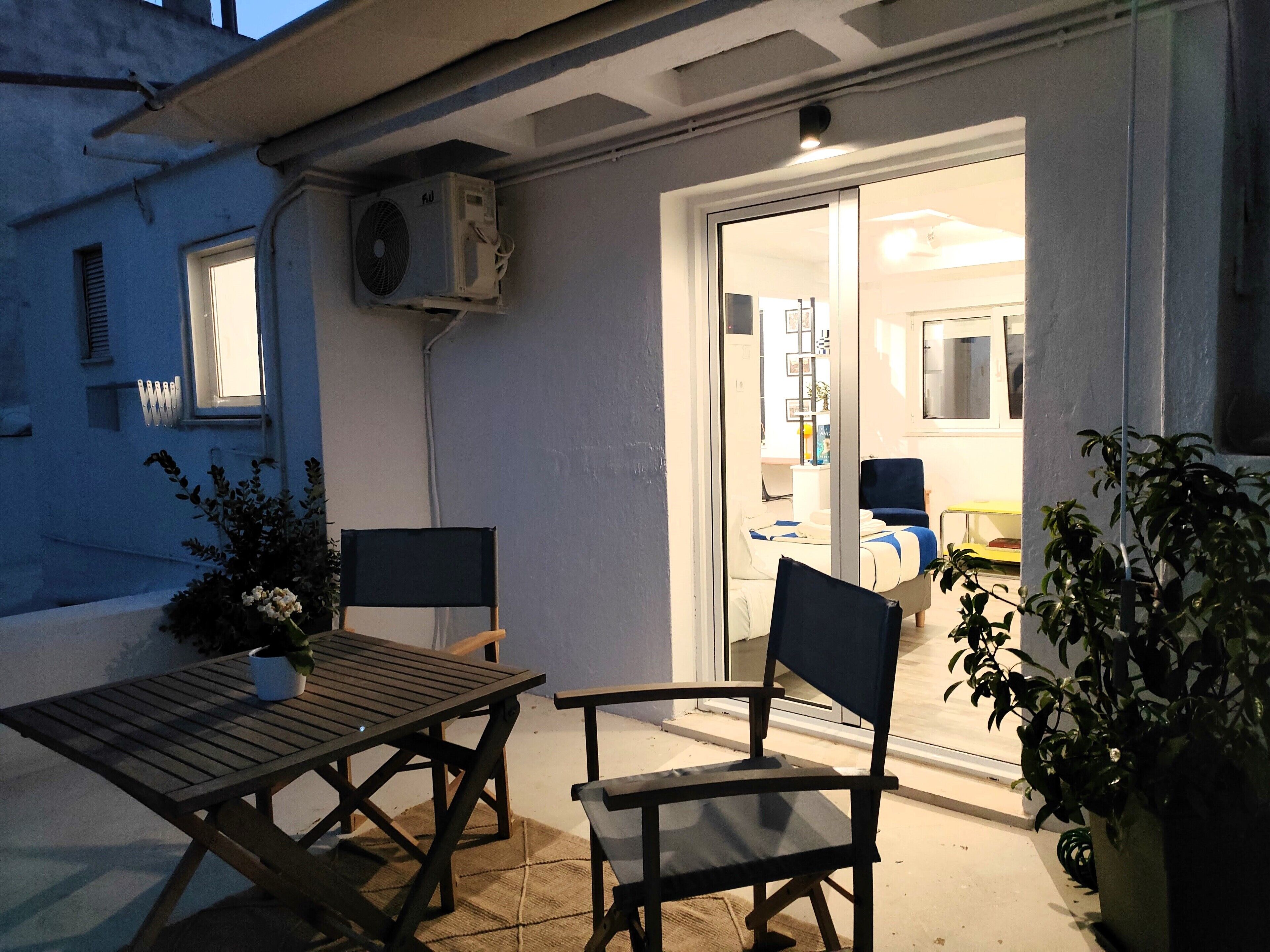 An outdoor patio area with a wooden table and chairs, a potted plant, and an air conditioning unit mounted on the wall.