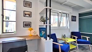 Een moderne kantoorruimte met een bureau, twee blauwe stoelen, een gele tafel en ingelijste foto's aan de muur.