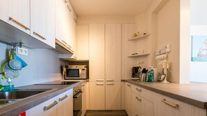 A compact kitchen with a microwave, stove, and sink. There are cabinets and a countertop with various items. - Apartment in Koksijde for 8 Person (Koksijde)
