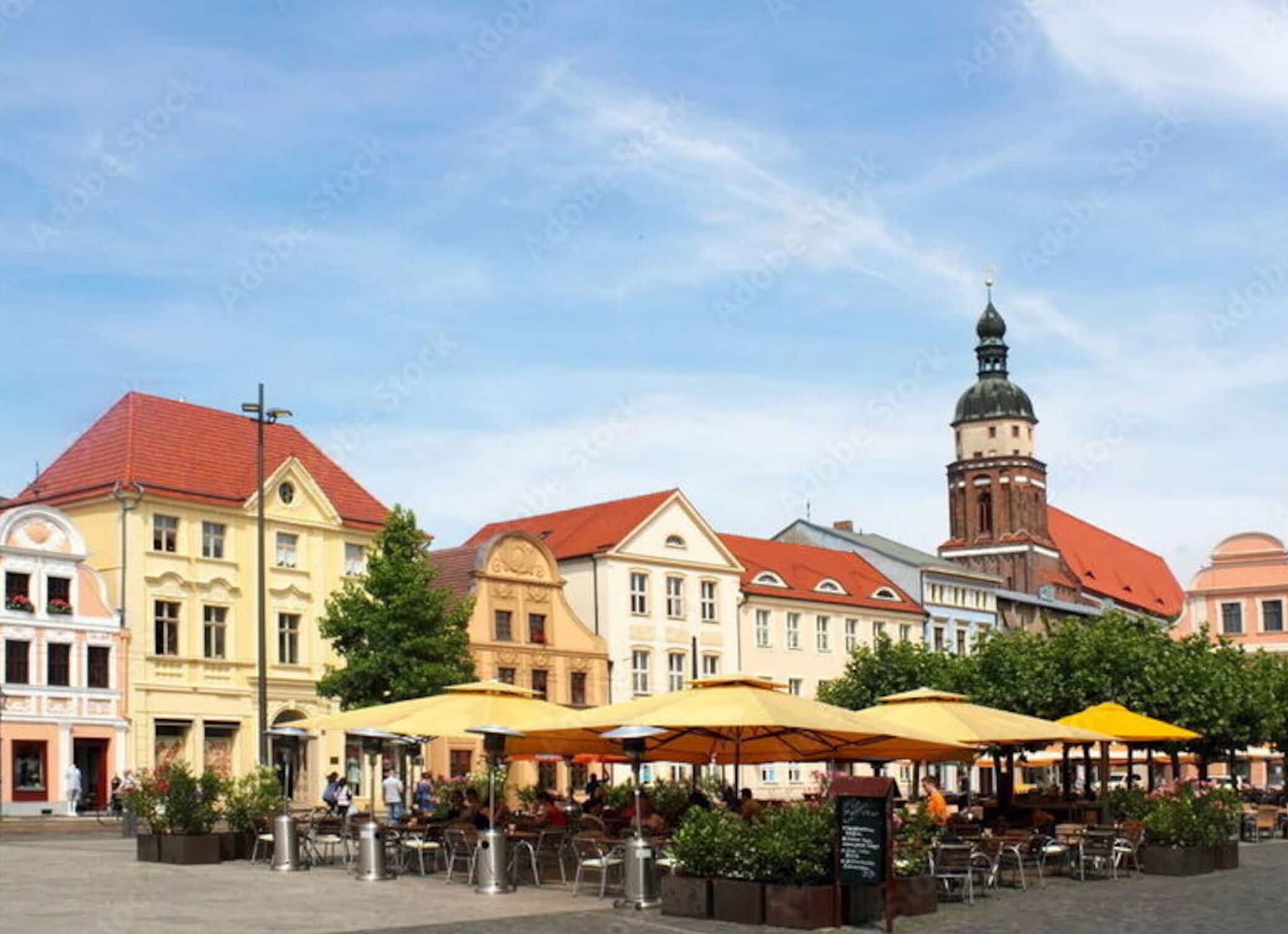 A square with outdoor seating, historic buildings, and a tower.