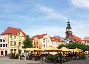 Une place agrémentée de terrasses, bordée de bâtiments historiques et surmontée d’une tour.
