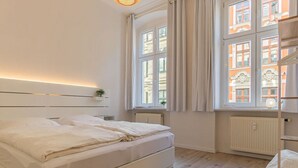 Une chambre à coucher avec un grand lit, une table de chevet avec une lampe, une fenêtre avec des rideaux et une vue sur les bâtiments à l’extérieur.