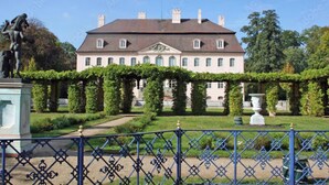 Un bâtiment imposant à la façade symétrique, agrémenté d’un jardin soigné et orné d’une statue classique en premier plan.