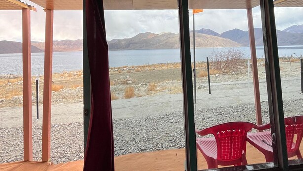 A room with a large window overlooking a lake and mountains. - Padma Cottage Pangong (Leh)