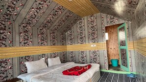 A room with a sloped ceiling, a bed with a red blanket, a wooden nightstand, and a small window with a view of the outside. - Padma Cottage Pangong (Leh)