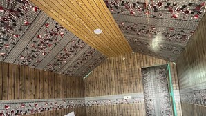A room with a wooden ceiling, a bed with a red blanket, and a bathroom with a blue bucket. - Padma Cottage Pangong (Leh)