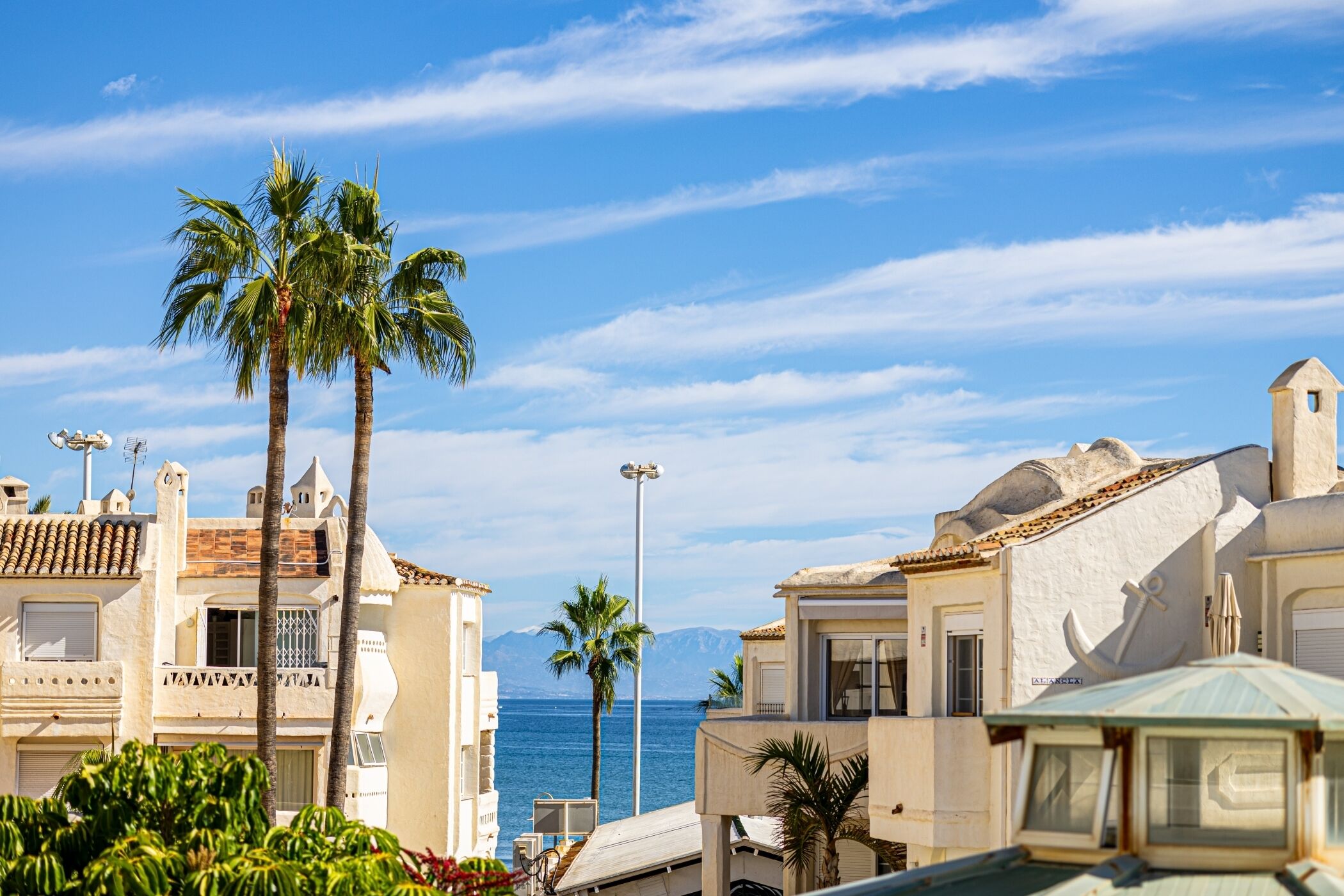 Un bâtiment situé sur la côte, offrant une vue sur la mer, des palmiers et un ciel dégagé.