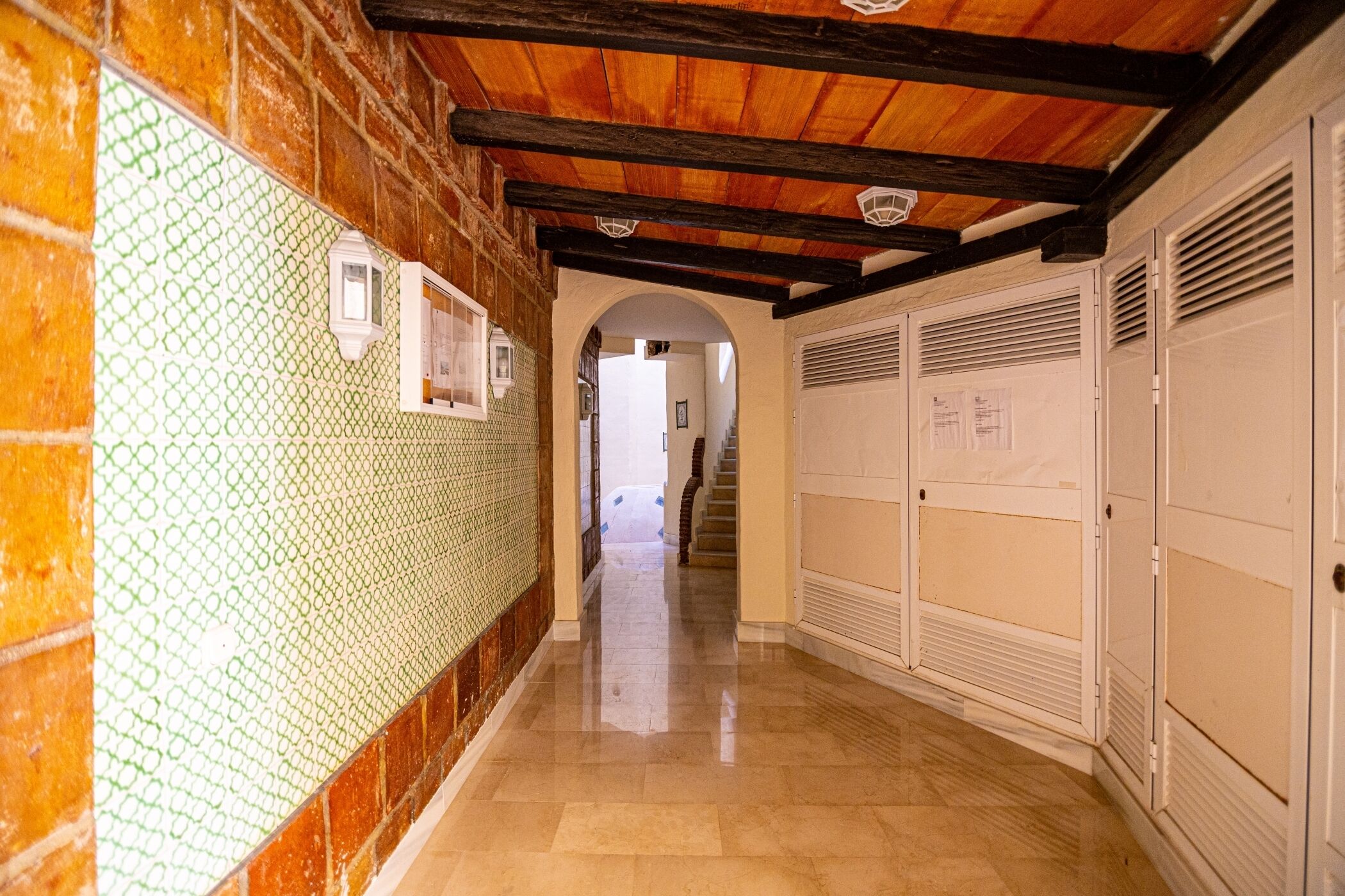 Un pasillo con pared de azulejos, vigas de techo de madera y suelo también de azulejos.