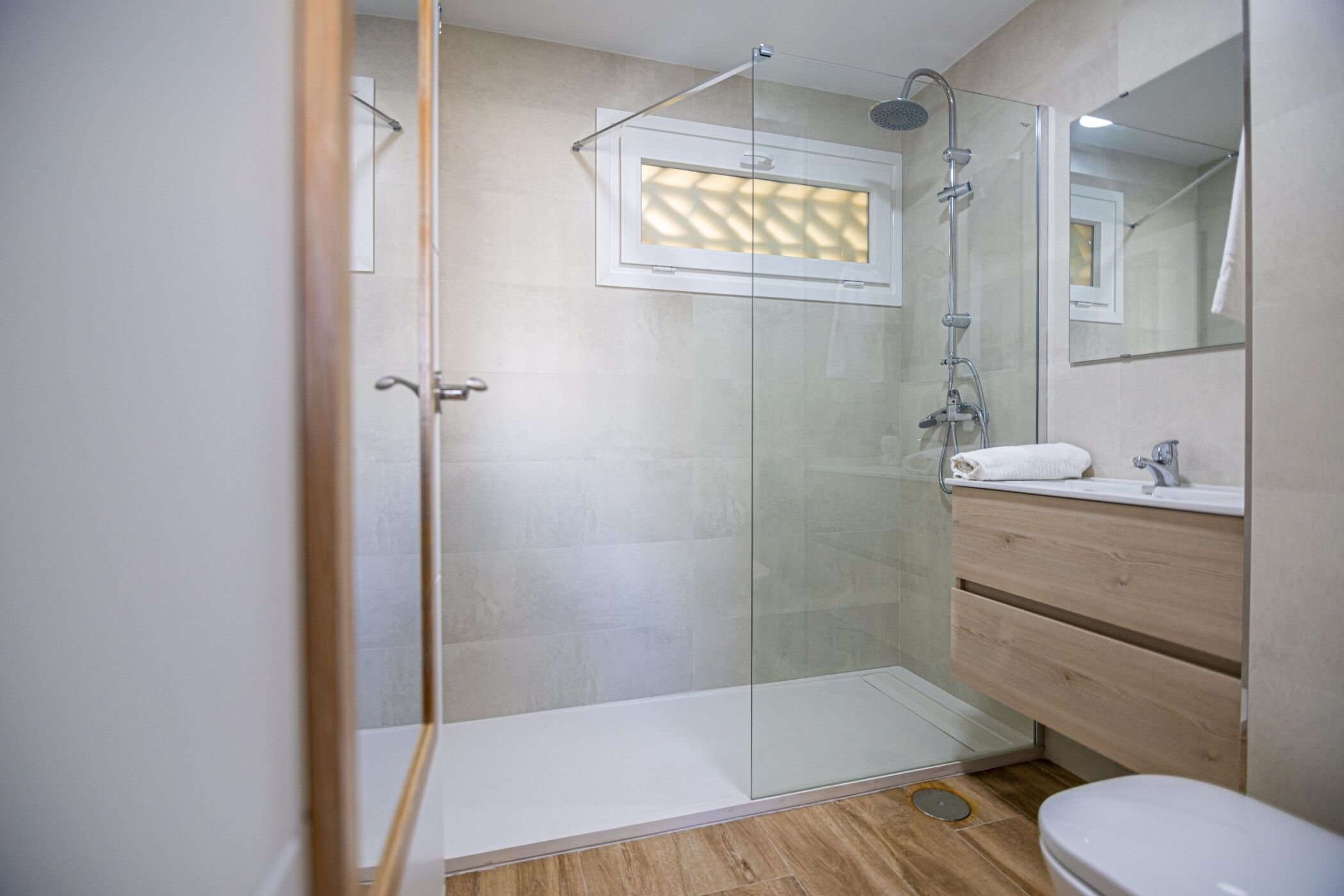 Un baño moderno con cabina de ducha de vidrio, tocador de madera y un inodoro blanco.