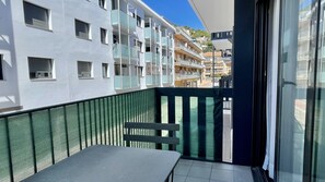 Ein Balkon mit Metallgeländer, einer Sitzbank und Blick auf mehrstöckige Gebäude.